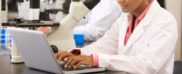 Male And Female Scientists Using Microscopes In Laboratory